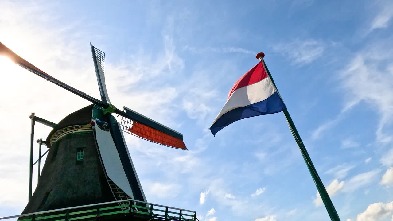 Rotating windmill and waving Dutch flag under bright blue sky, captured with smooth camera movement