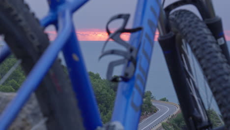 time lapse of mountain bike frame in front of a road bend as cars drive past while sun rises over the ocean in the background