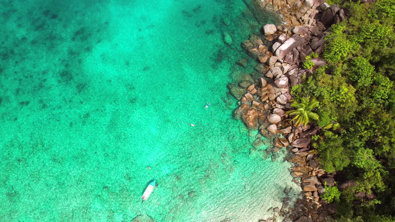 Drone pantai Anse Major, pandangan mata burung terbang di atas 4 turis snorkeling di dekat perahu, batu granit, air pirus, dan pantai berpasir putih, Mahe Seychelles 30 fps.