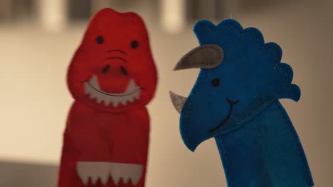 a red tyrannosaurus rex finger puppet and a blue triceratops talk together