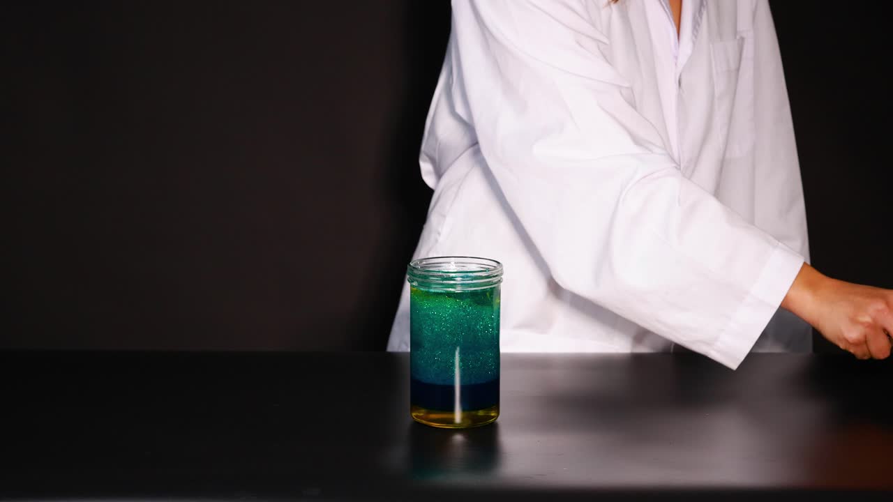 un científico con una bata de laboratorio lleva a cabo un experimento de hielo seco, mostrando reacciones químicas en un vaso con colores vibrantes