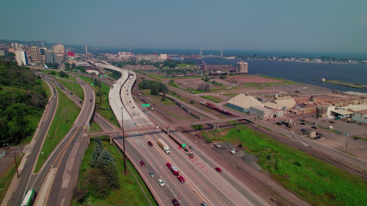 Interstate 35 running along the Duluth waterfront with active traffic, road work cones, rail lines, silos, and Lake Superior a summer day