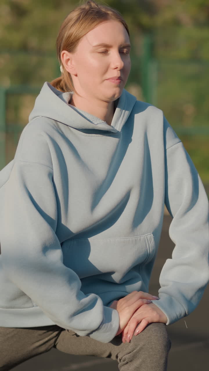 푸른 스웨터를 입은 운동 선수가 야외에서 운동하는 부분적인 모습. 흐릿한 배경에는 초록색, 바 울타리, 다른 사람이 앉아있는 좌석이 있으며, 운동과 피트니스를 강조합니다.