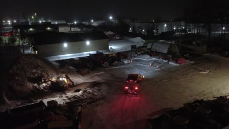 excavator and emergency road transit vehicle stockpiling salt for snow removal at night with flashing safety lights