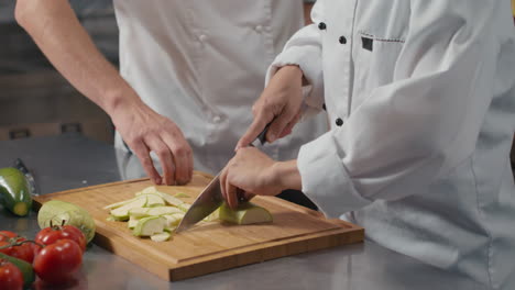 chef teaching young cook to cut vegetables