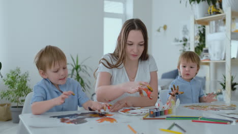 the family has fun painting on paper with their fingers in paint. mom and two children paint with fingers on paper