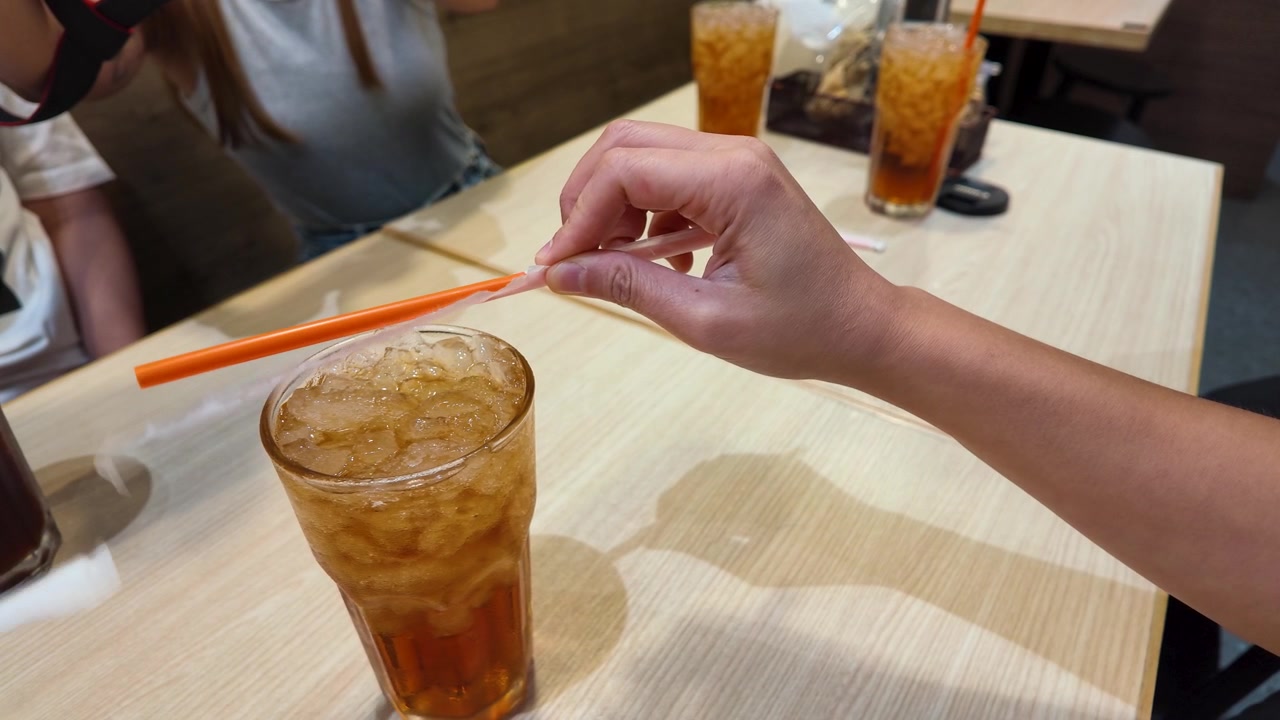 Cận cảnh đôi tay tháo vỏ bọc nhựa khỏi ống hút trên ly trà đá ở Bangkok