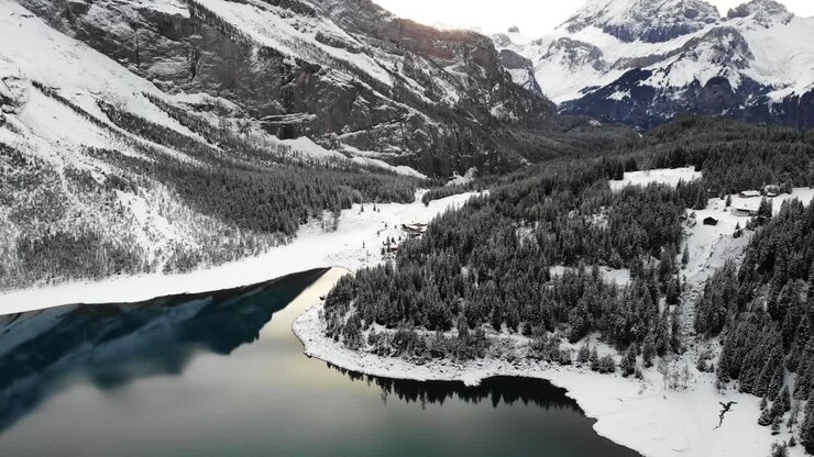Sorvolo aereo sulle rive del lago Oeschinensee a Kandersteg, Svizzera, in una fredda giornata invernale con alberi coperti di neve