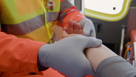 close up view of a paramedic touching the hand of a patient lying on a stretcher inside an ambulance