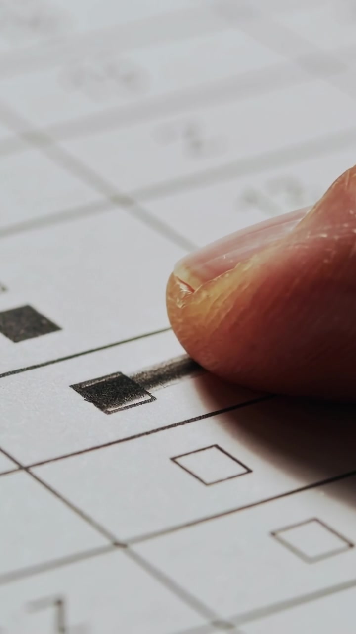 Vertical video: Hovering, pressing right fingertip onto filled square on paper grid, smudging toner