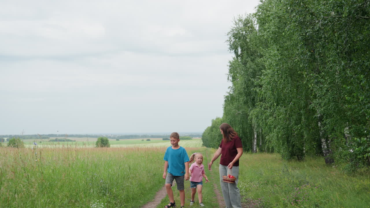 Smiling family walking through sunny field, Happy mother and children exploring nature during summer day, Joyful family moment captured outdoors with bright smiles amidst trees and open space