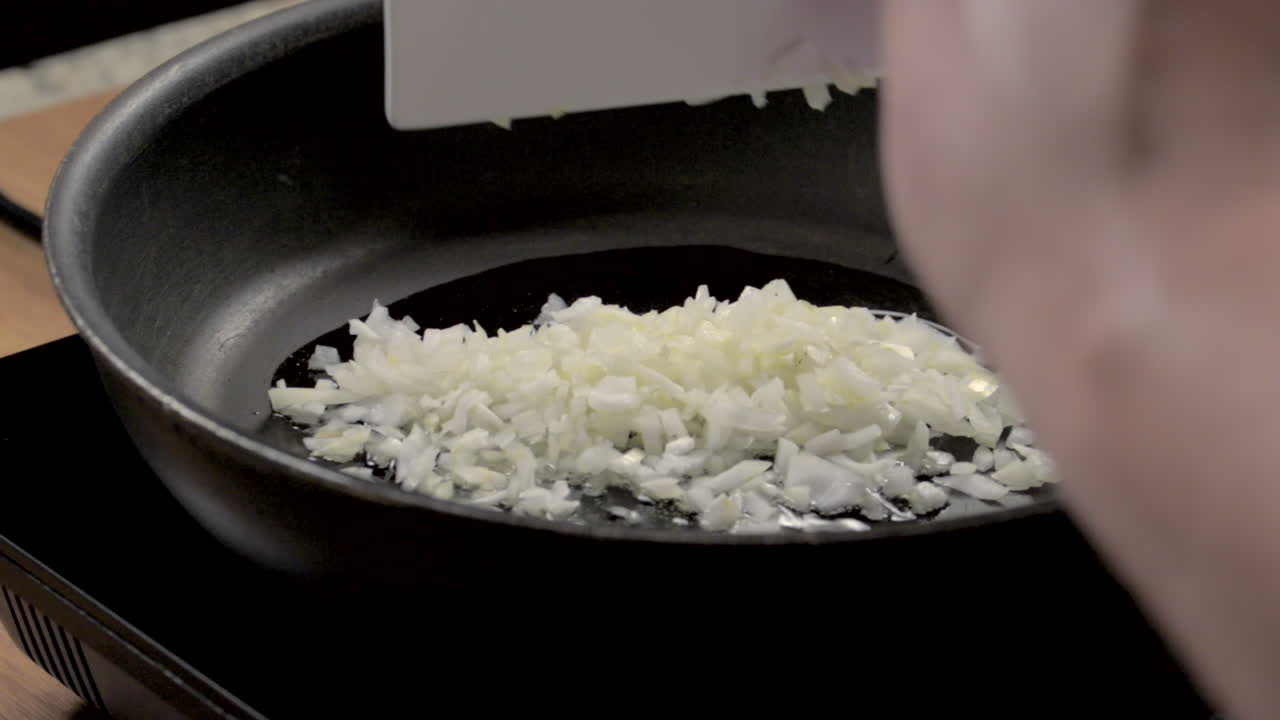 verter cebolla picada sobre el aceite en una sartén caliente
