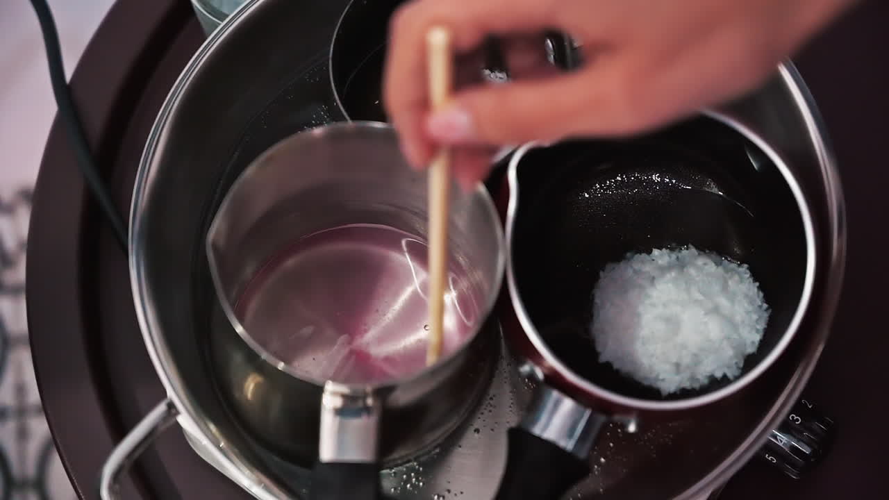 Hand made candles production, female hand mixing melting wax in pots. Slow motion