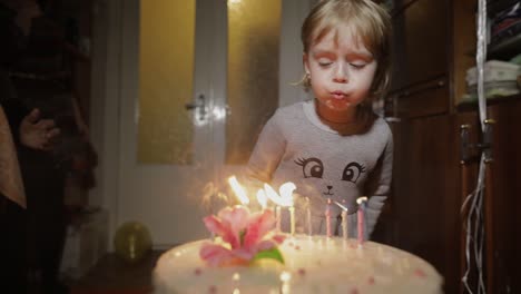 little cute girl blows out candles on birthday cake at home party