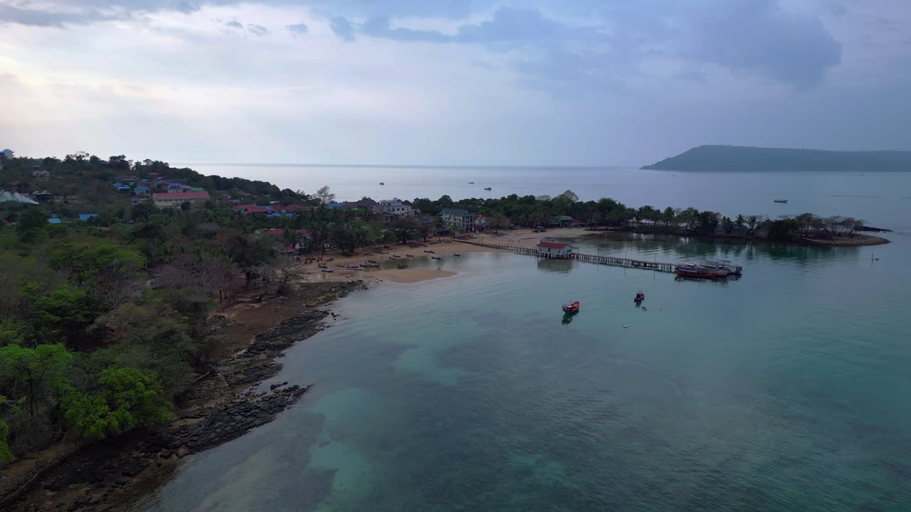 Koh Rong Sanloem island village in Cambodia, featuring turquoise water, pier, boats and tropical jungle. Smooth aerial view flight drone shot footage from above