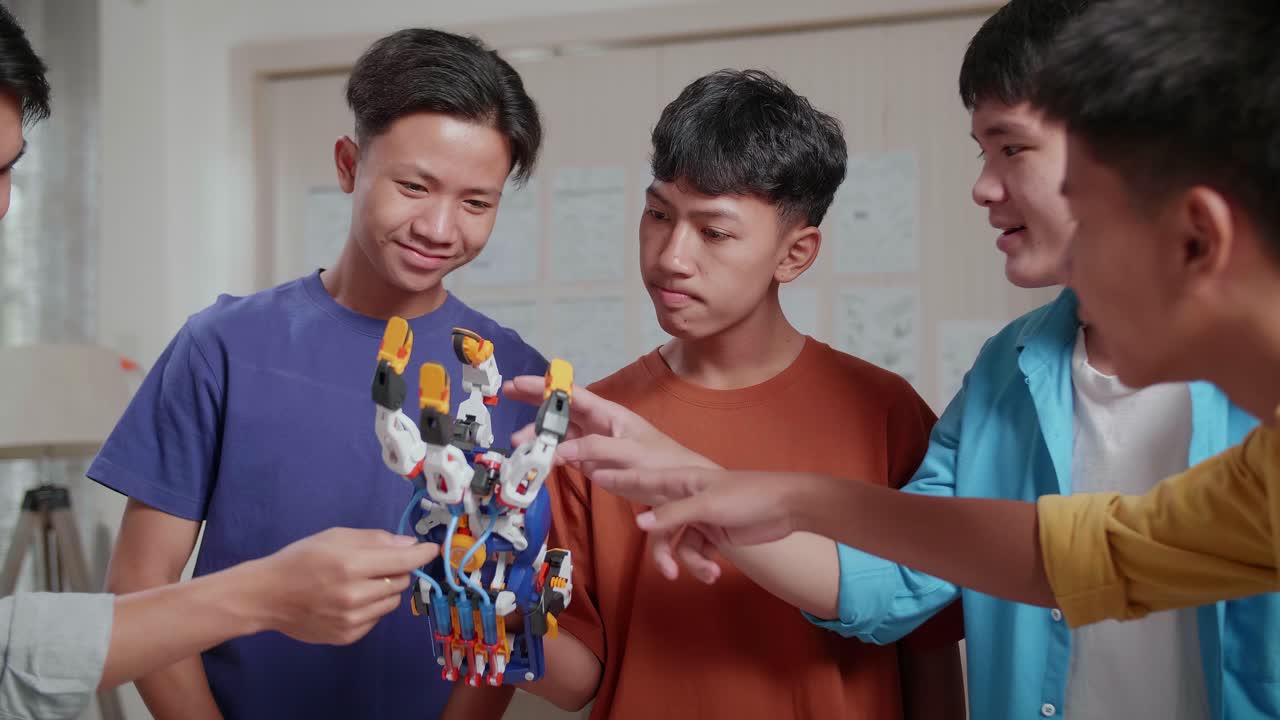 노트북과 3d 프린팅을 가진 젊은 아시아 소년 그룹이 사이보그 손을 확인하고 집에서 일하는 성공을 축하합니다.