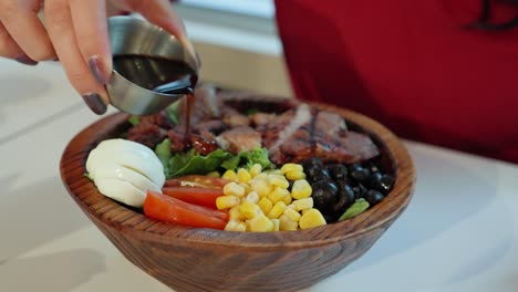 mujer vertiendo salsa oriental sobre ensalada de cerdo a la parrilla en tazón de madera