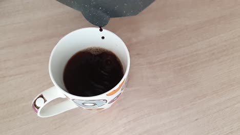 Pouring-hot-black-coffee-into-white-cup-with-colorful-donuts-from-moka-pot-in-slowmotion