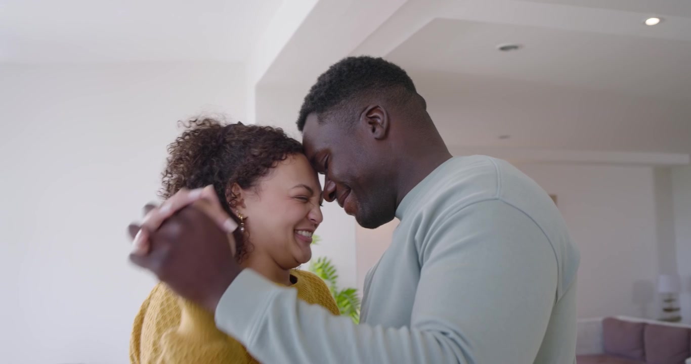 African American couple holding hands, swaying, touching heads at home in knits, sharing affection