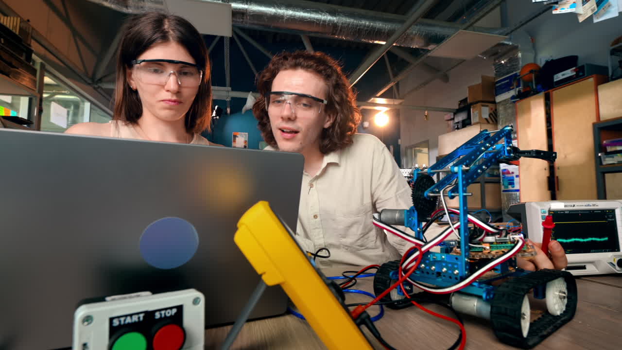Young man and woman in protective glasses doing experiments in robotics in a laboratory using a computer. Robot and tools on the table