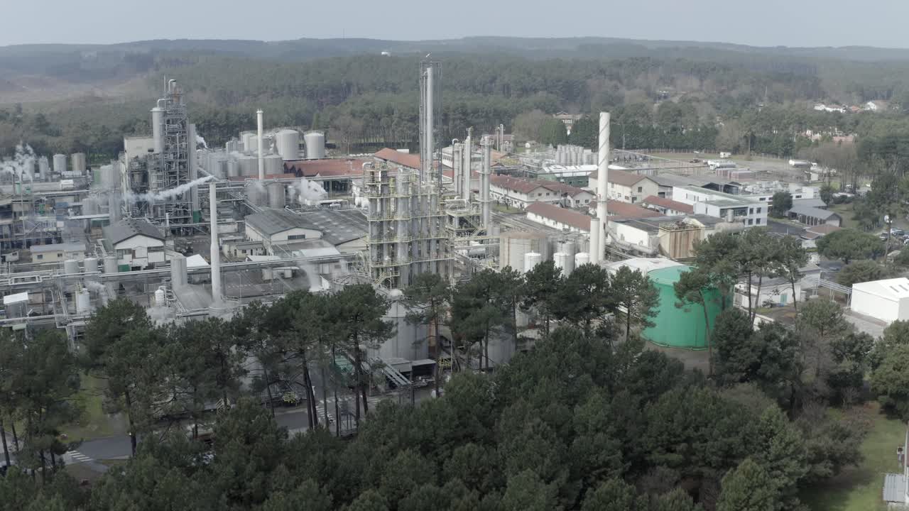 Industrial complex with steam rising from stacks, contrasted with surrounding forest, Vielle-Saint-Girons, France. Aerial forward descending