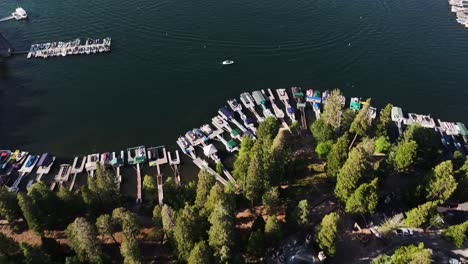 Der-Sonnenuntergang-über-Dem-Pfeilspitzendorf-Und-Dem-Jachthafen-Des-Sees-Zeigt-Den-Blick-Von-Den-Berghäusern-Auf-Den-See-Voller-Boote,-Die-Sich-Schnell-Fortbewegen,-In-Orangefarbenen-Farben.-Luftwagen-Neigen-Sich-Nach-Oben