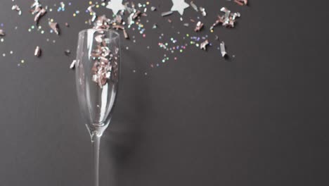 video of champagne flute glass, with glitter confetti and silver stars on black, with copy space