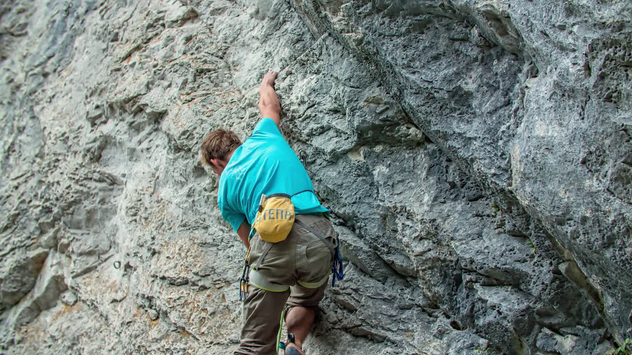 Young adventurous mountaineer, climbing the steep and rocky mountain. Concept of adventure and extreme sports. View from below