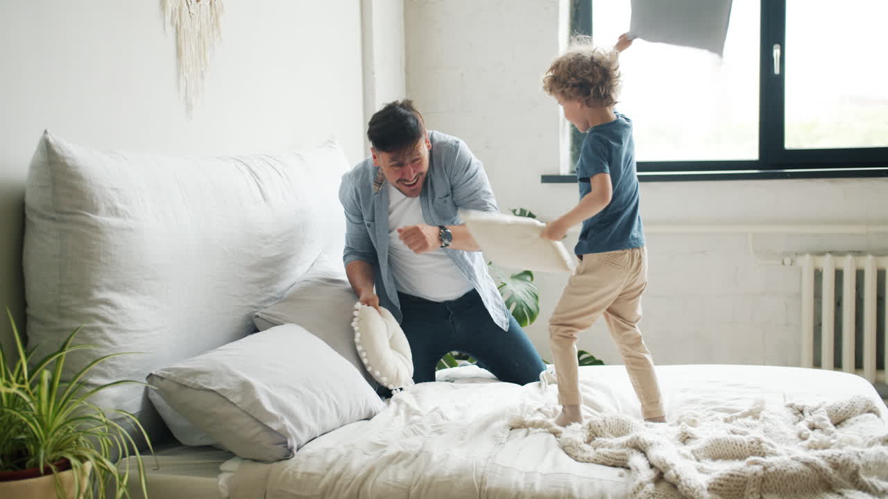 Father and Son Having a Pillow Fight in the Bedroom