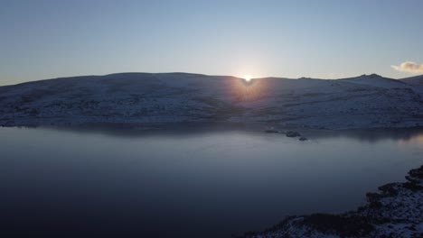flyover lagoa comprida dam, sunset flare picking through snow covered hill, serra da estrela