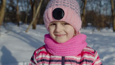 Joyful-little-child-girl-looking-at-camera,-smiling,-fooling-around,-making-faces-in-winter-park