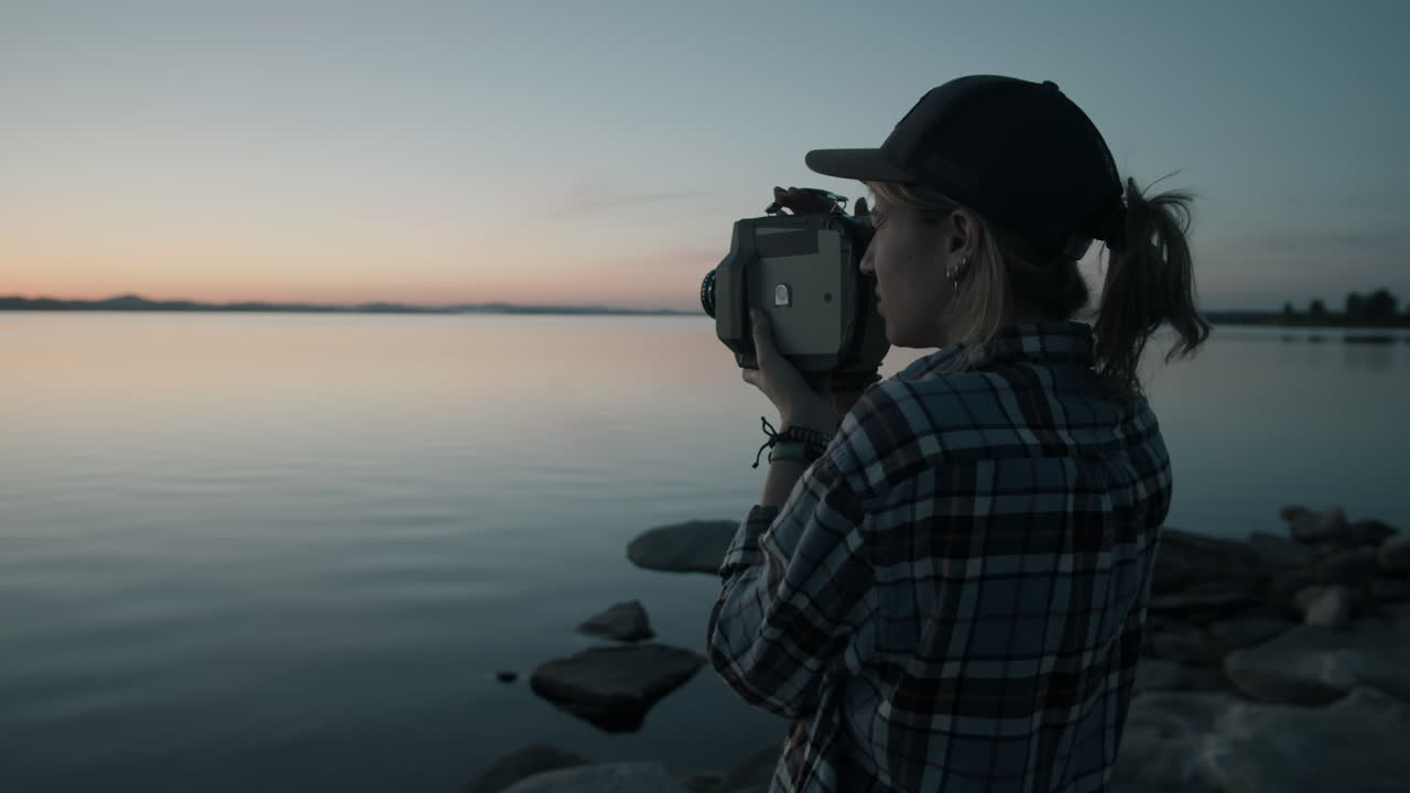 Woman Filming Sunset over Lake with Vintage Video Camera