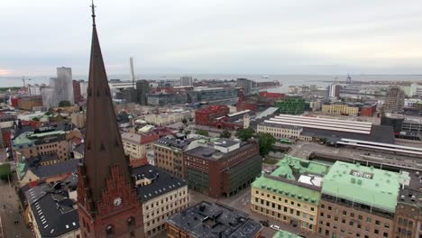 aerial view of church tower spire, flying down in front of church in malmö city. cityscape buildings in the background