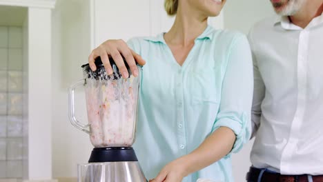 Couple-preparing-fruit-smoothie-in-kitchen