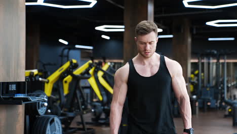 tired sportsman rest after hard workout. muscular man in black singlet in modern fitness center. handsome athlete in gym.