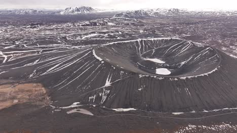 majestic aerial view of hverfjall crater near lake mývatn, iceland. a stark volcanic cone dusted with snow stands amid rugged lava fields in a dramatic winter landscape.