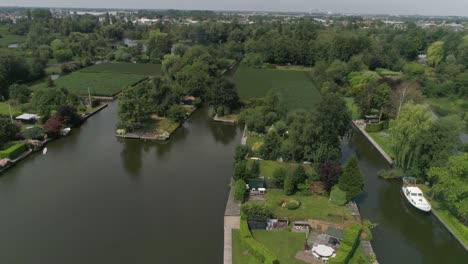 aerial slomo of dutch countryside surrounded with small rivers, green trees and bushes,with small town in background