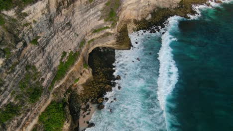 aerial view ascending shot, waves hitting the rocky shore of the tanjung ringgit cliff, green grass and trees in the background