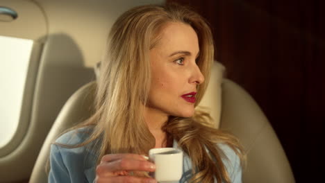 smiling businesswoman enjoy coffee in golden sunlight on private jet closeup.