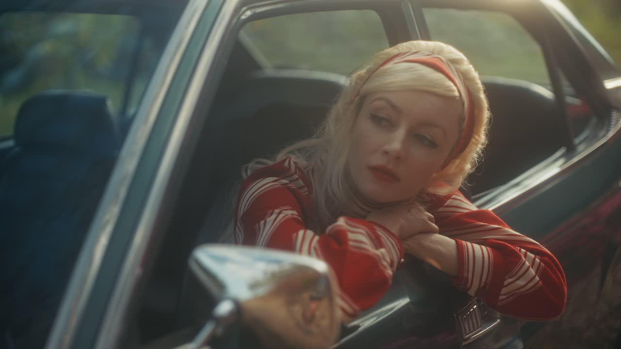 Nachdenkliche blonde Frau in einem Oldtimer, die aus dem Fenster schaut