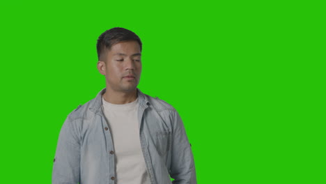 Studio-Shot-Of-Casually-Dressed-Young-Man-Ignoring-Mobile-Phone-Call-Against-Green-Screen-