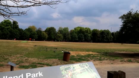 Holland-Park-Sportplatzschild-Mit-Menschen,-Die-Im-Hintergrund-Spiele-Spielen