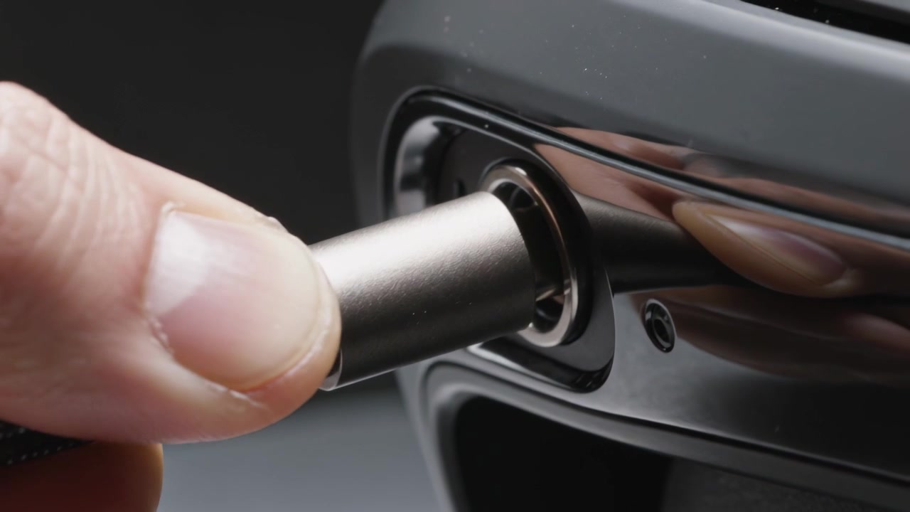 Mão alinhando e inserindo conector metálico na porta de um dispositivo preto brilhante, com parafuso.