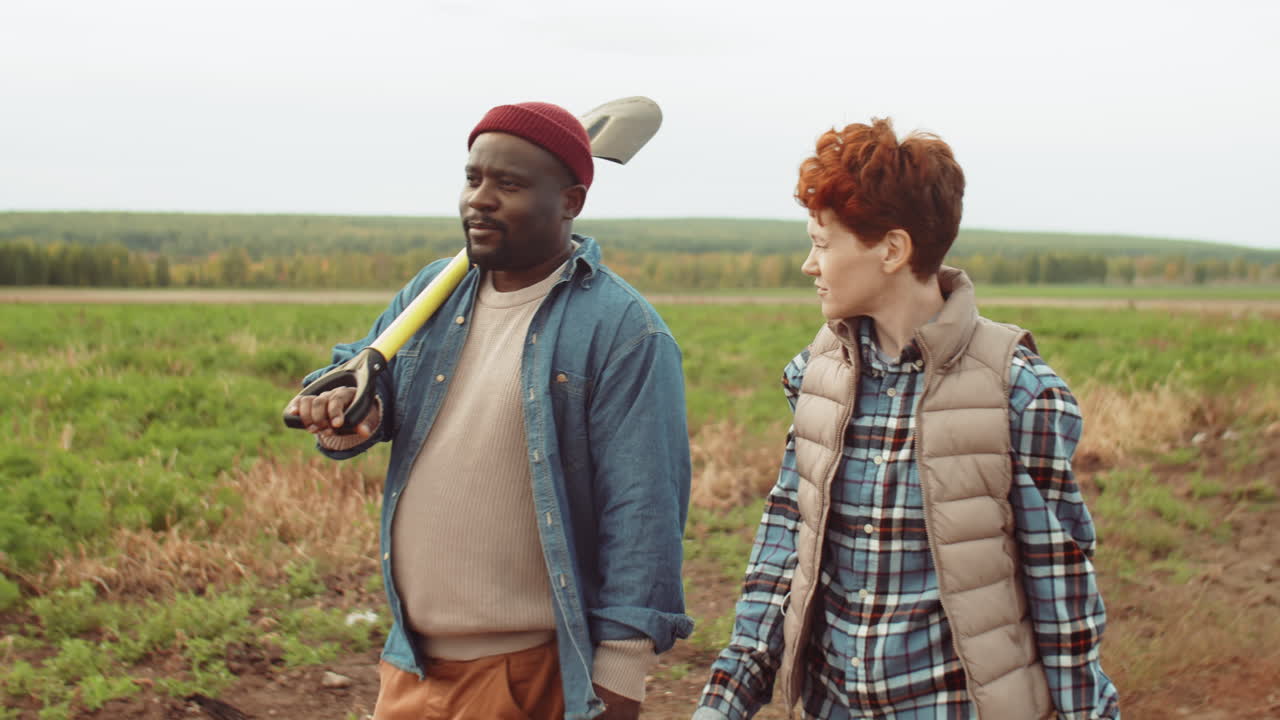 многонациональные фермеры, идущие с инструментами по полю и разговаривающие