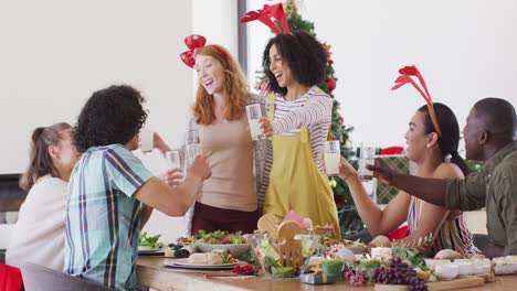 Happy-group-of-diverse-friends-sitting-at-table-and-eating-dinner-together,-making-toast