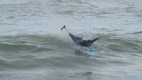 hombre deportivo en traje de neopreno con pierna artificial surfeando en el océano