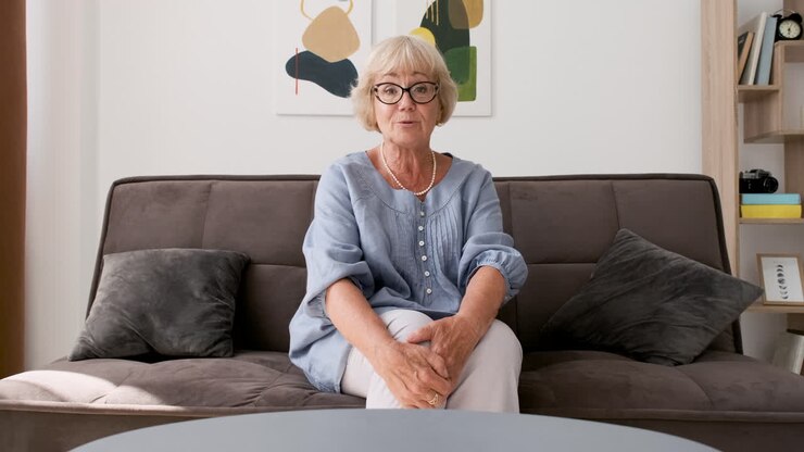 Smiling Senior Woman Sitting On Sofa In Living Room Looking At Camera During A Video Call