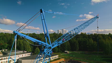 rear strut, front strut, jib and pendant of a blue luffing construction crane against a blue sky and clouds with forest in background