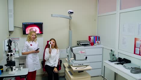 modern ophthalmological center interior. young specialist is examining woman's eyes in clinic. female patient closes her eyes in turns with occluder.