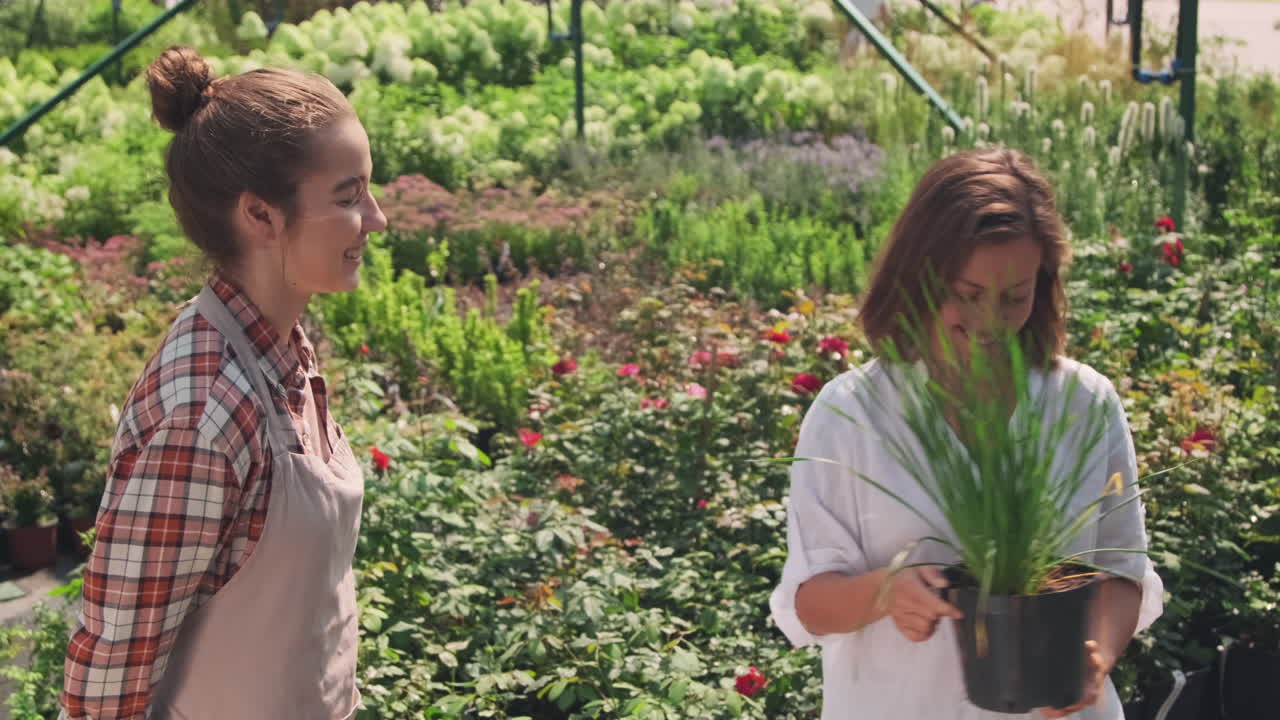 Two women interact over plants in a greenhouse